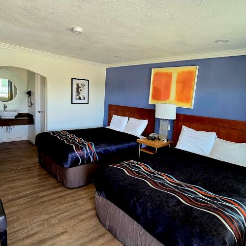 A hotel room with two double beds, a TV, a small table, and an open bathroom area with a mirror.