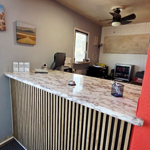 The image shows a small reception area with a marble counter, chairs, a fan, and wall art. It's a compact, well-lit office space.