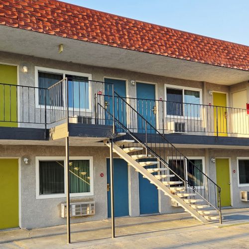 This image shows a two-story motel with colorful doors, an exterior staircase, and a red roof under a clear sky.