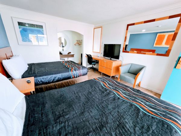 A modern hotel room with two beds, desk, chair, and a TV. There's a large mirror and a painting on the wall.
