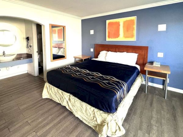 A neatly made bed with a blue and tan comforter in a modern bedroom featuring a blue accent wall, side tables, and a nearby sink area.